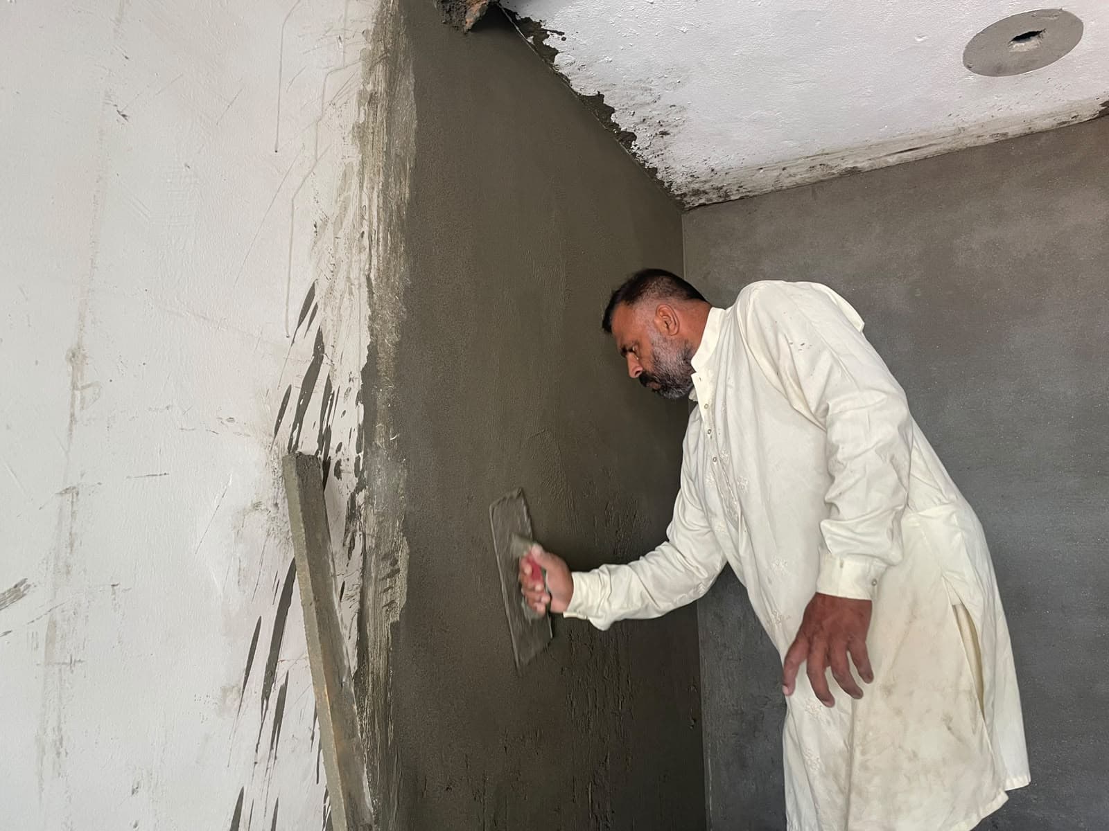 A worker replastering a wall at House #162