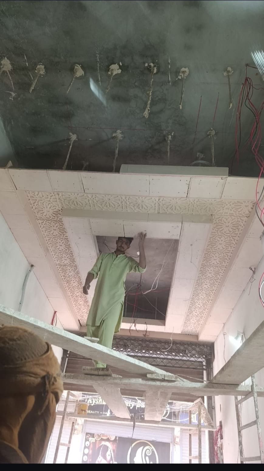 A worker on a scaffold beside a newly fitted carved ceiling border
