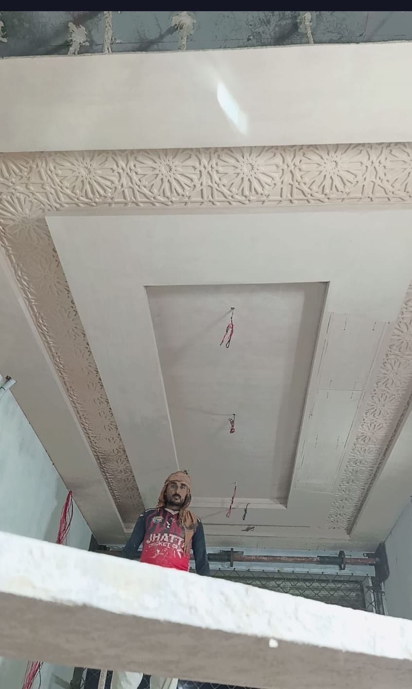 The finished carved border framing a recessed ceiling, with a worker below