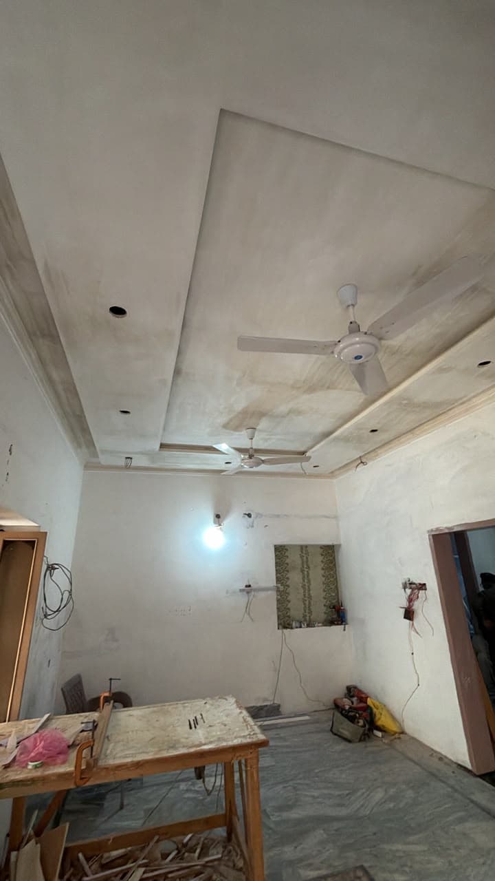 A false ceiling with a recessed border and a ceiling fan, in a room under renovation