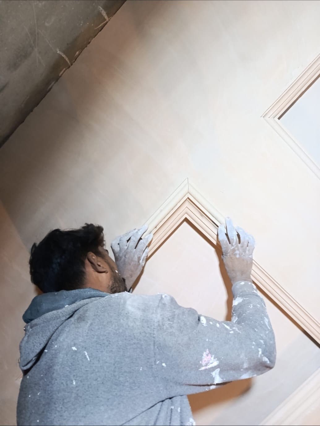 A worker fitting a decorative moulding to a wall