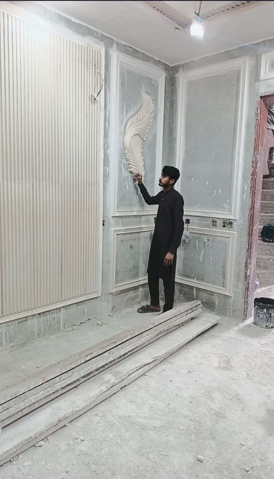 A worker shaping a carved feature beside fluted wall panels
