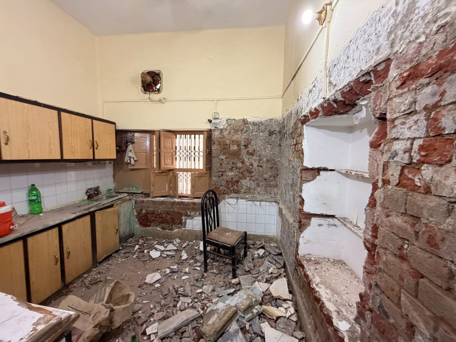 A kitchen with old wall tiles stripped back to the brick, rubble on the floor