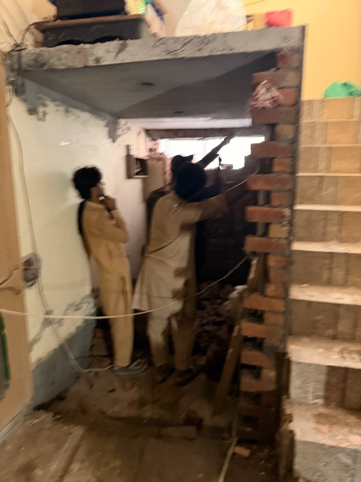 Two workers building a new brick wall beside the staircase