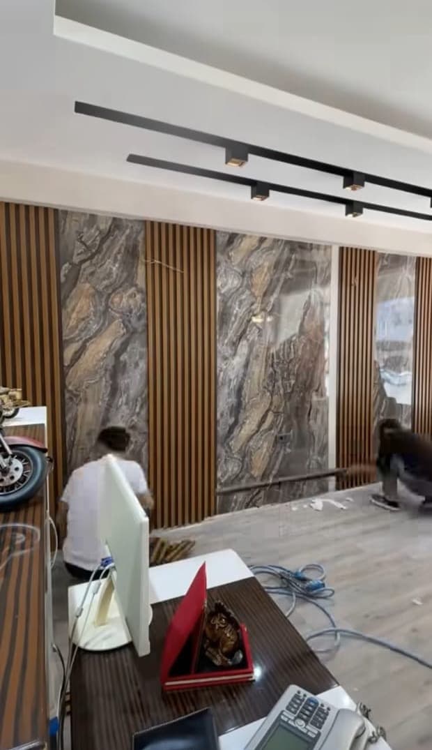 Workers fitting stone-effect sheets between wooden fluted panels, with track lights above