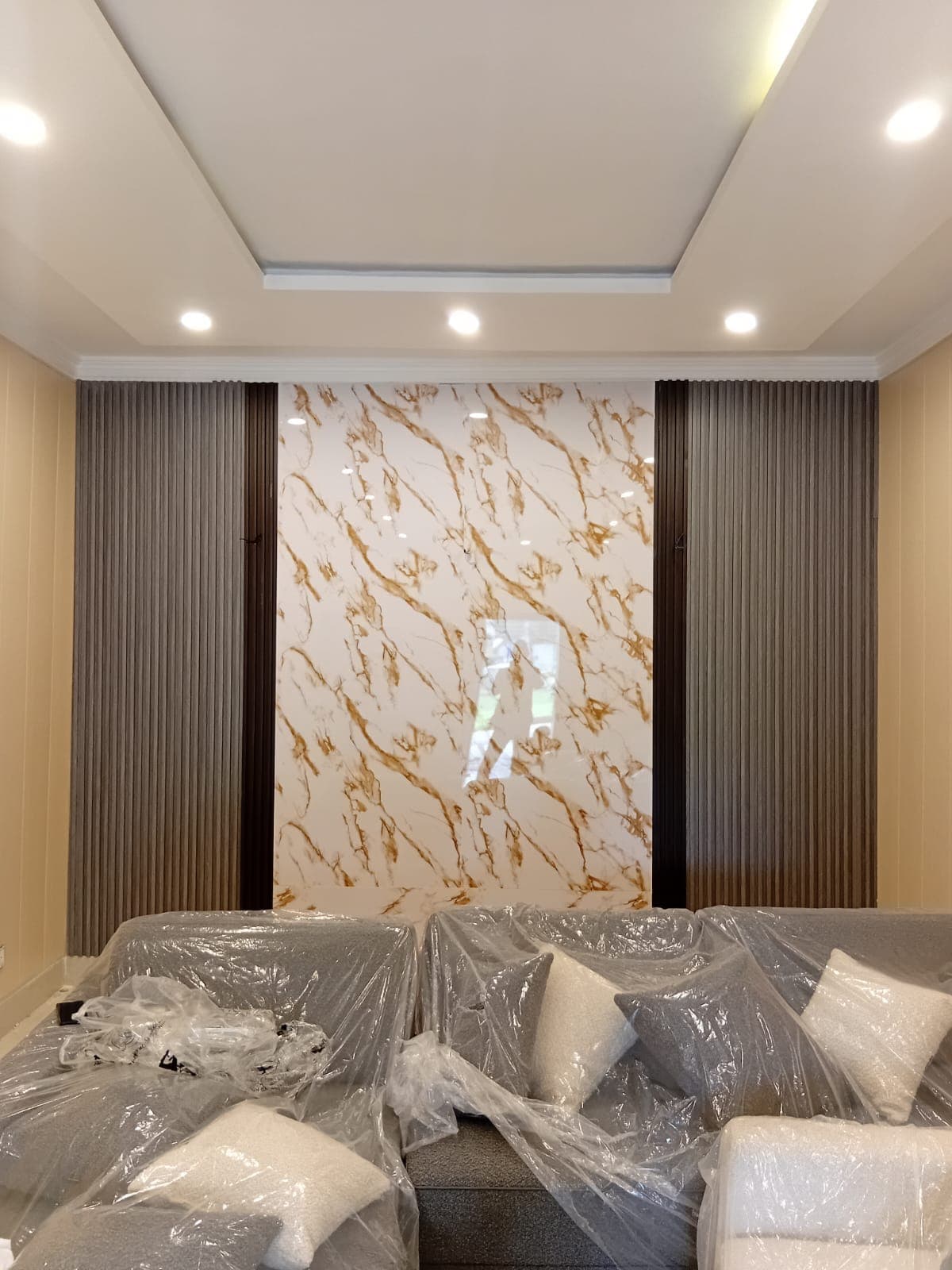 The finished media wall: a marble-effect centre panel between dark fluted panels, under downlights