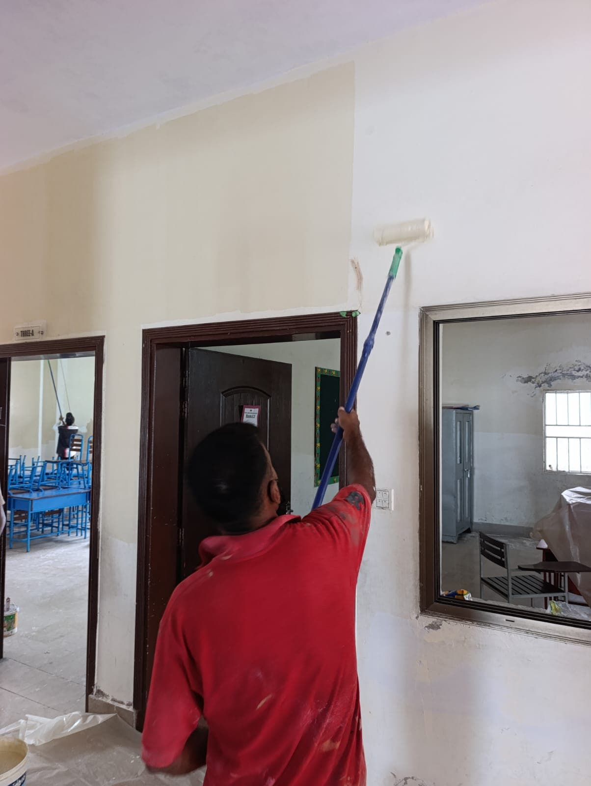 A painter rolling fresh paint high on a classroom wall