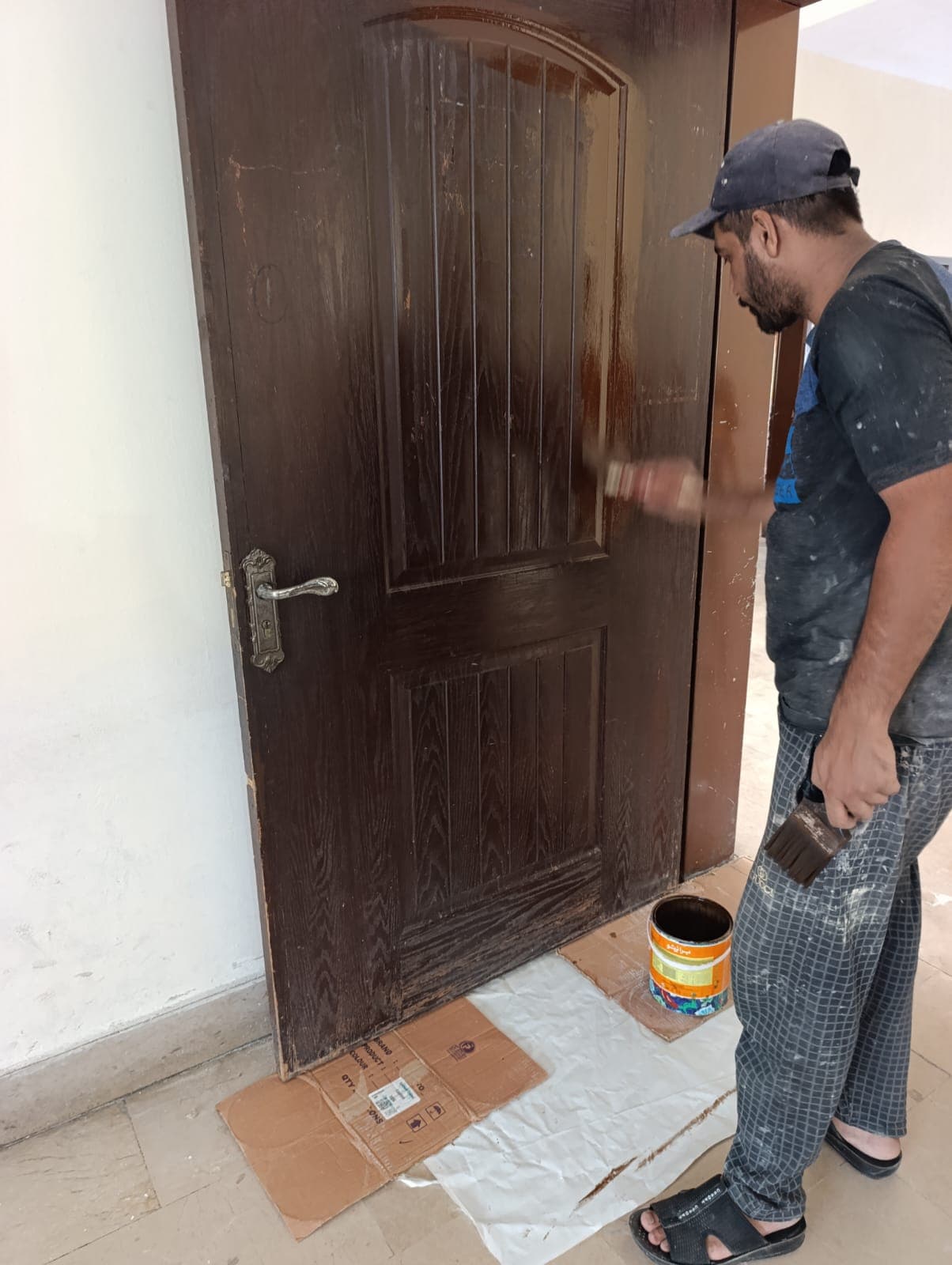 A painter brushing polish onto a panelled wooden door over protective sheets