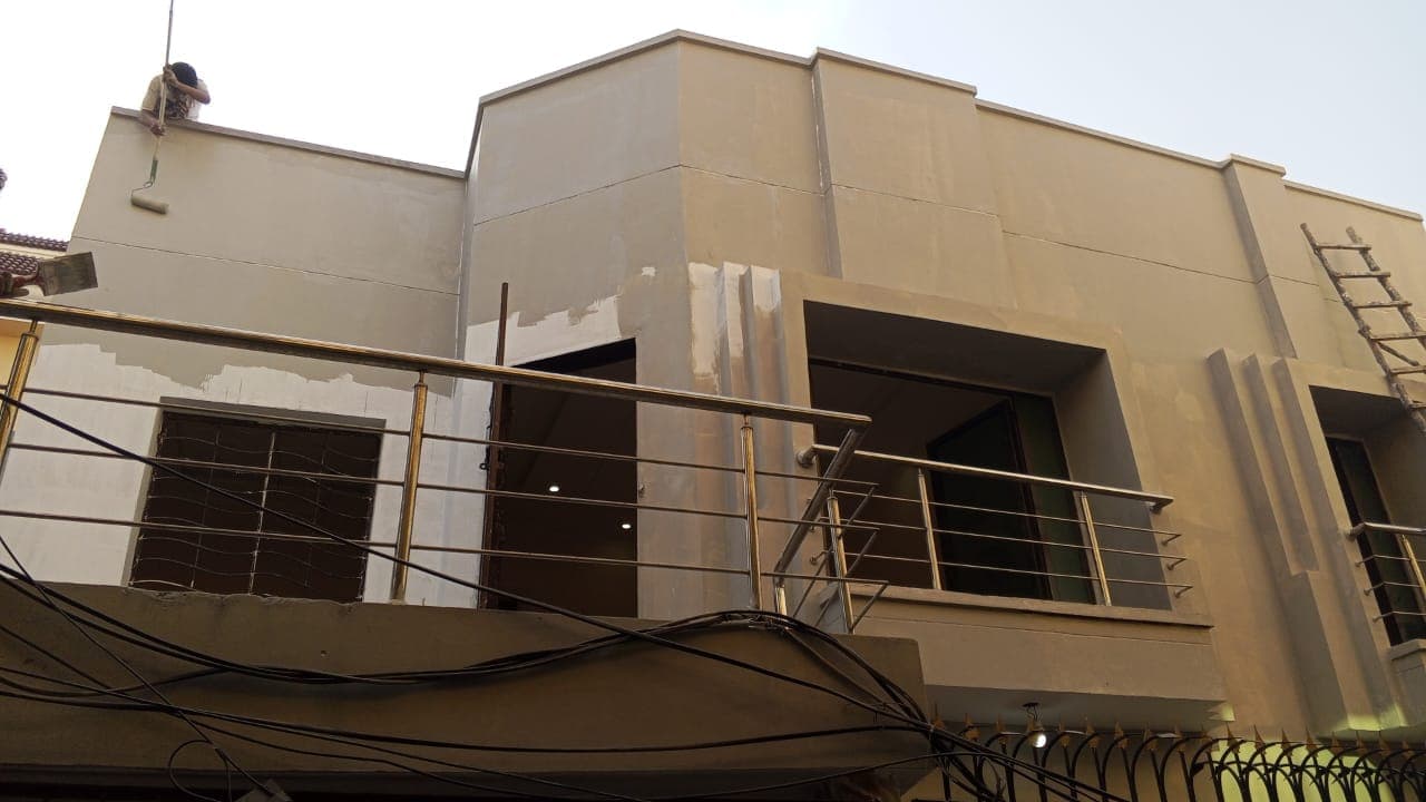 A house front with bare, patched plaster and filler marks, workers on the roof