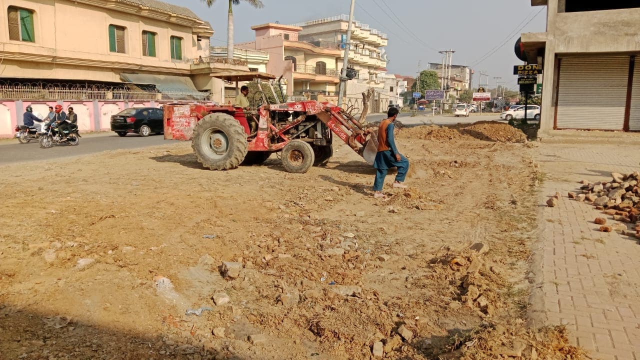 A tractor and worker levelling earth next to a paved footpath