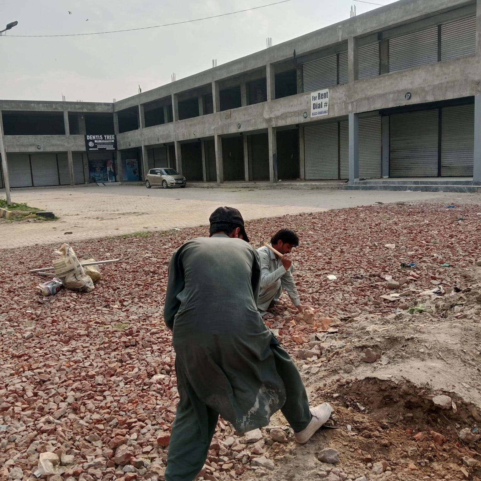 Two workers levelling the brick base in front of the shop row