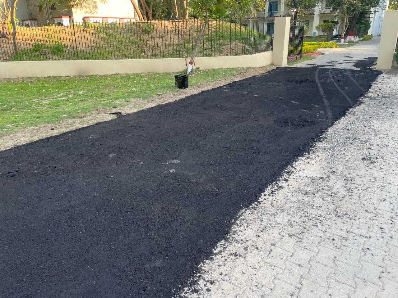 A finished asphalt patch along a road edge beside a fenced lawn