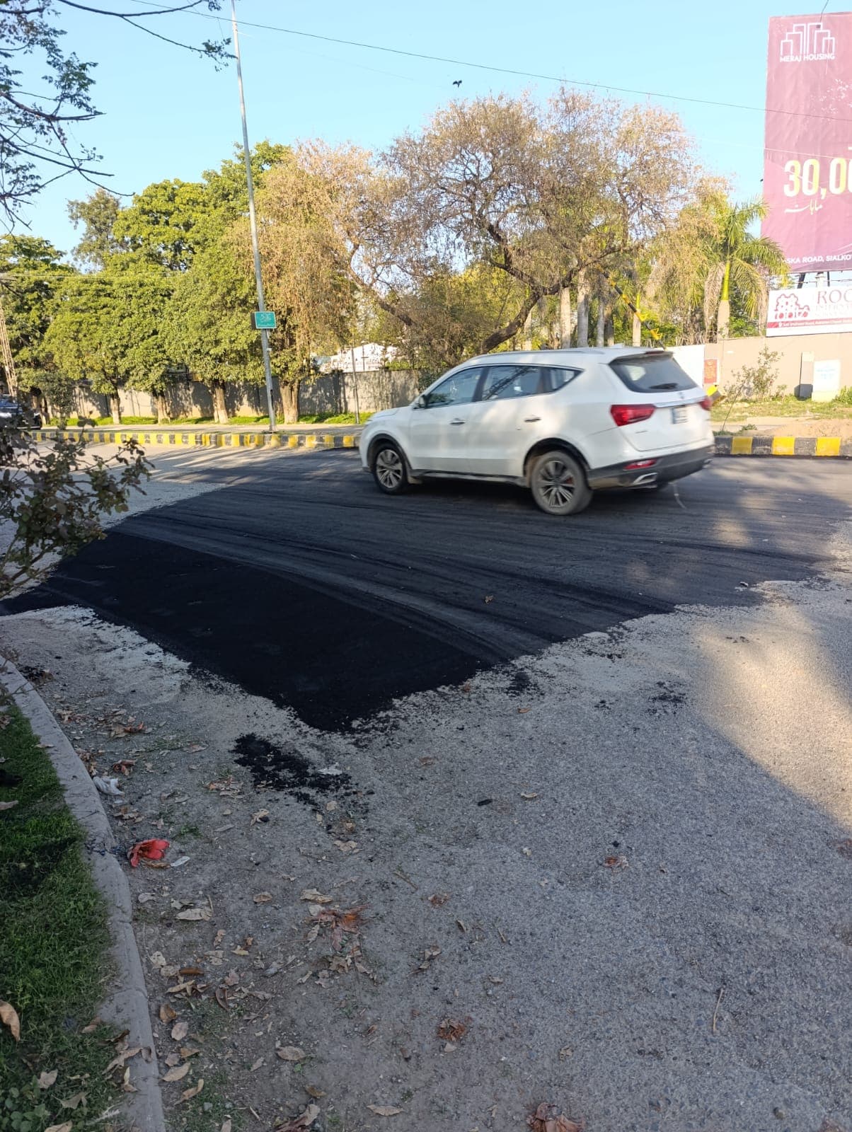 A finished asphalt patch at a roundabout, with a car driving over it
