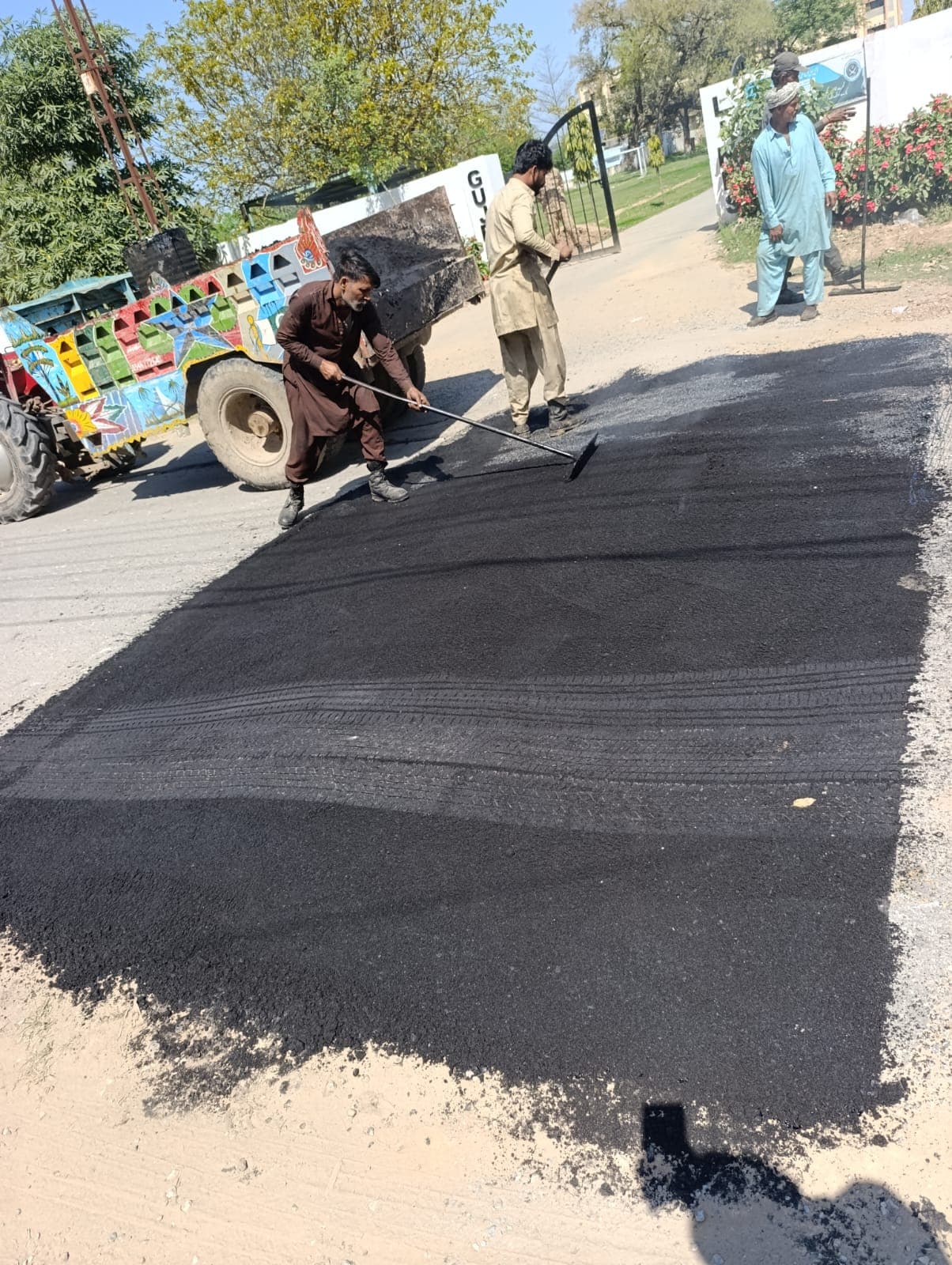 Workers finishing the edge of a smooth, rolled asphalt patch next to a tractor