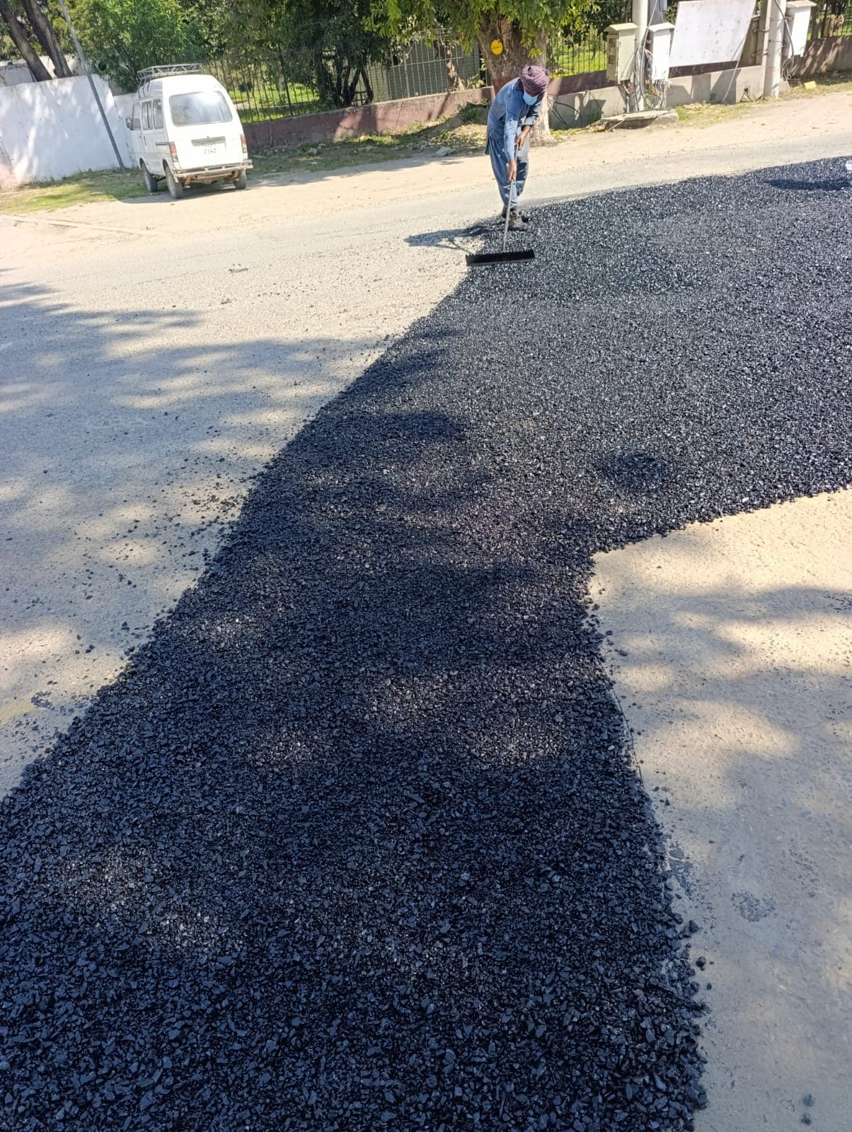 A worker levelling a wide asphalt patch with a rake