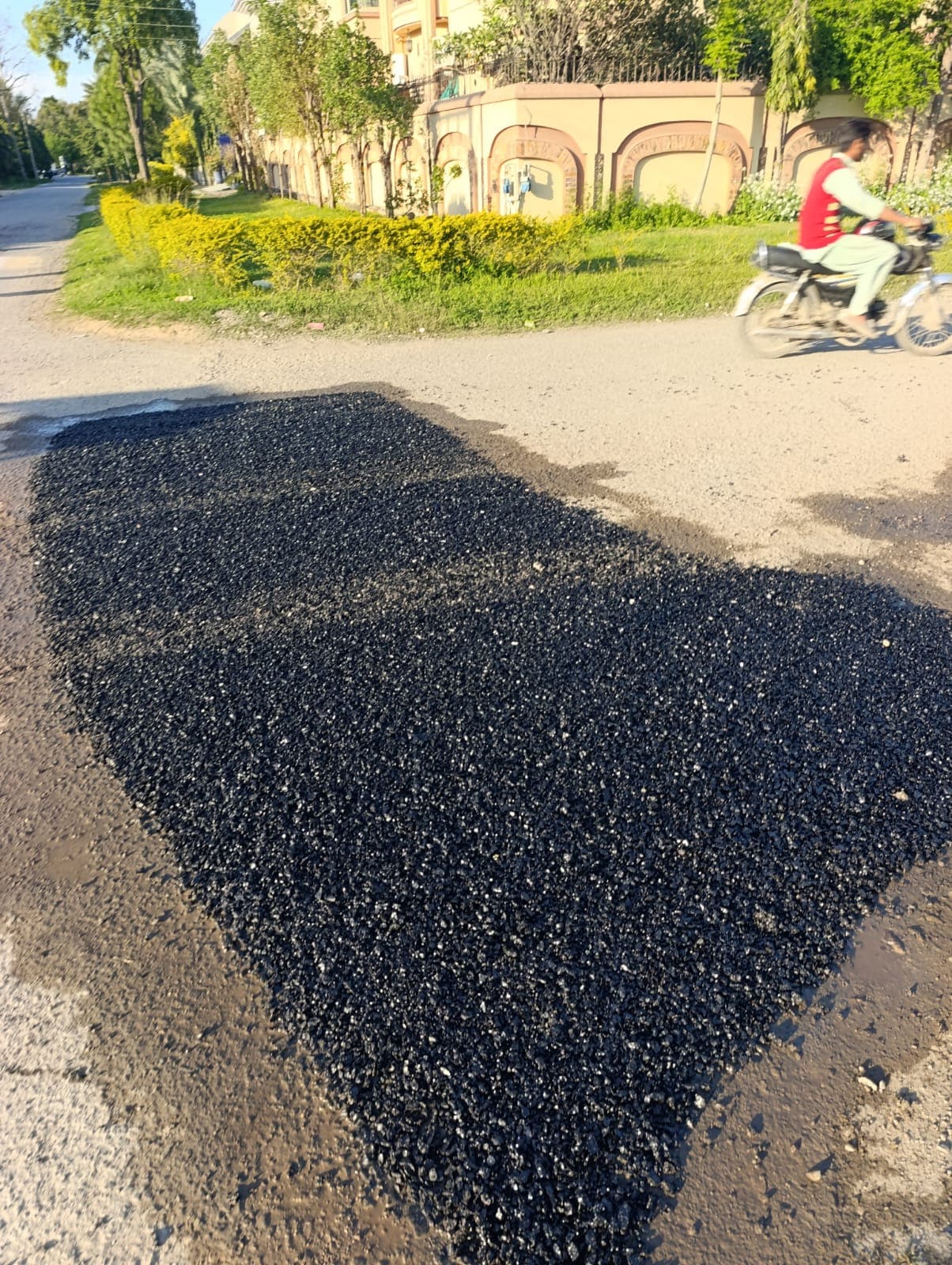 A patch of loose asphalt at a road junction, with a motorcyclist passing