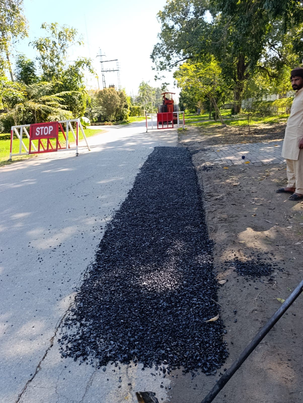 A narrow strip of fresh asphalt beside a stop barrier, with a roller waiting behind