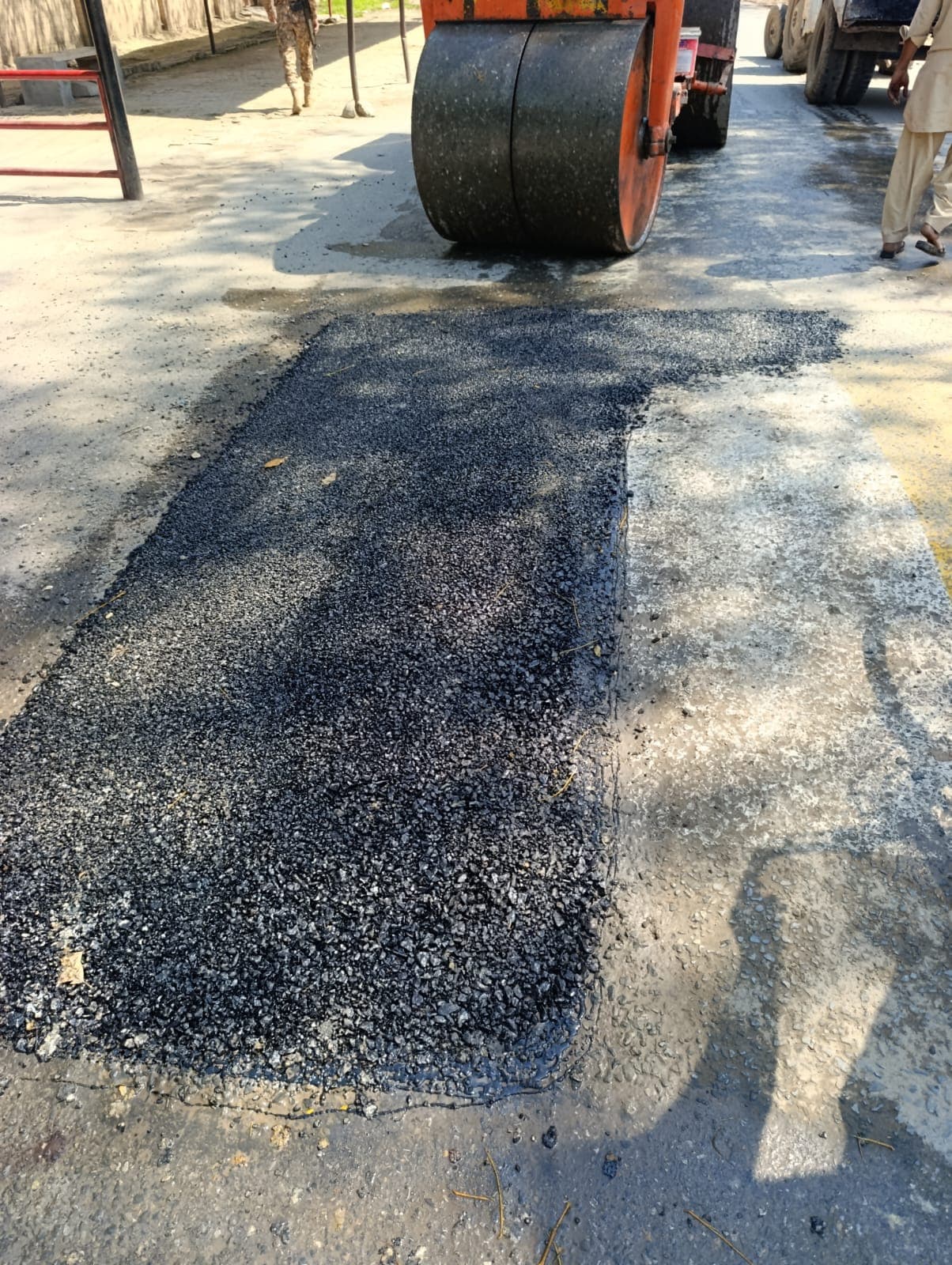 A road roller compacting a long asphalt patch in the shade