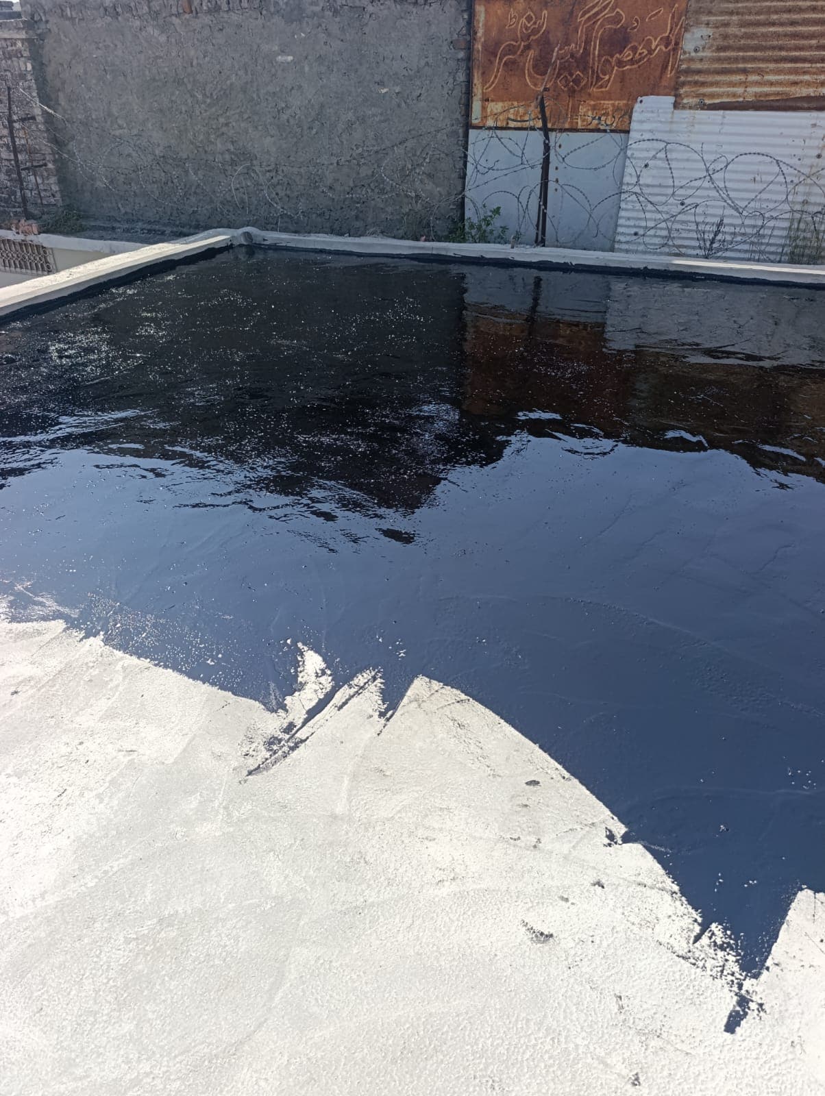 A flat roof half covered in a fresh, glossy black bitumen coat