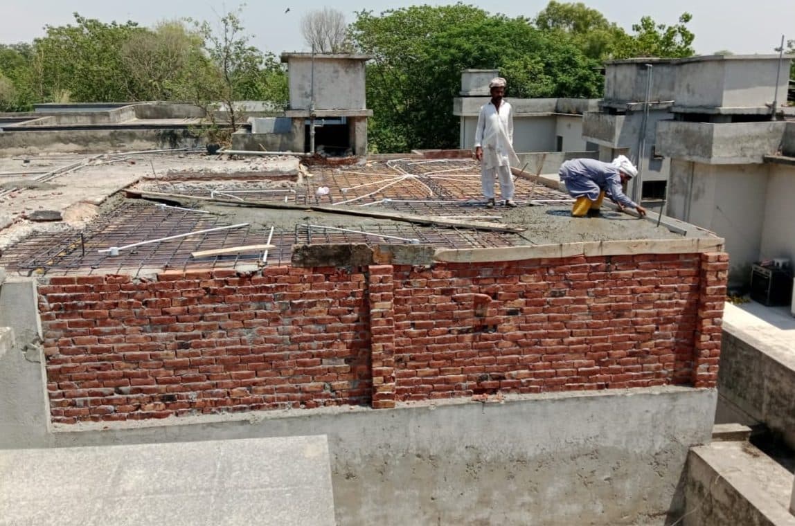 Workers laying steel reinforcement and conduits on a roof over brick walls