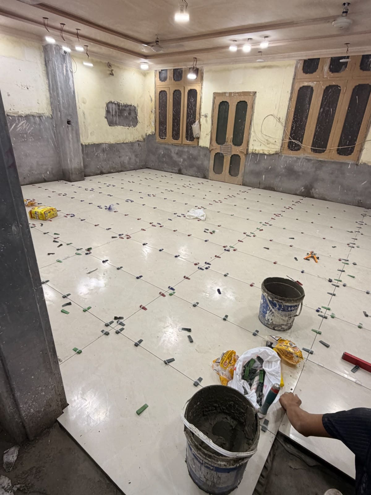 A worker laying large glossy tiles with levelling clips across a hall