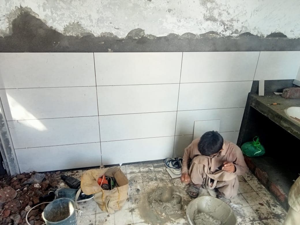 A worker tiling the lower part of a kitchen wall in white