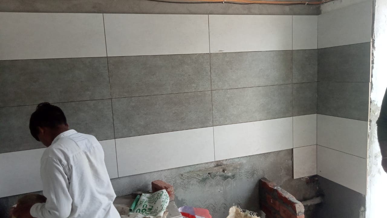 A worker fitting grey and white wall tiles above a kitchen counter
