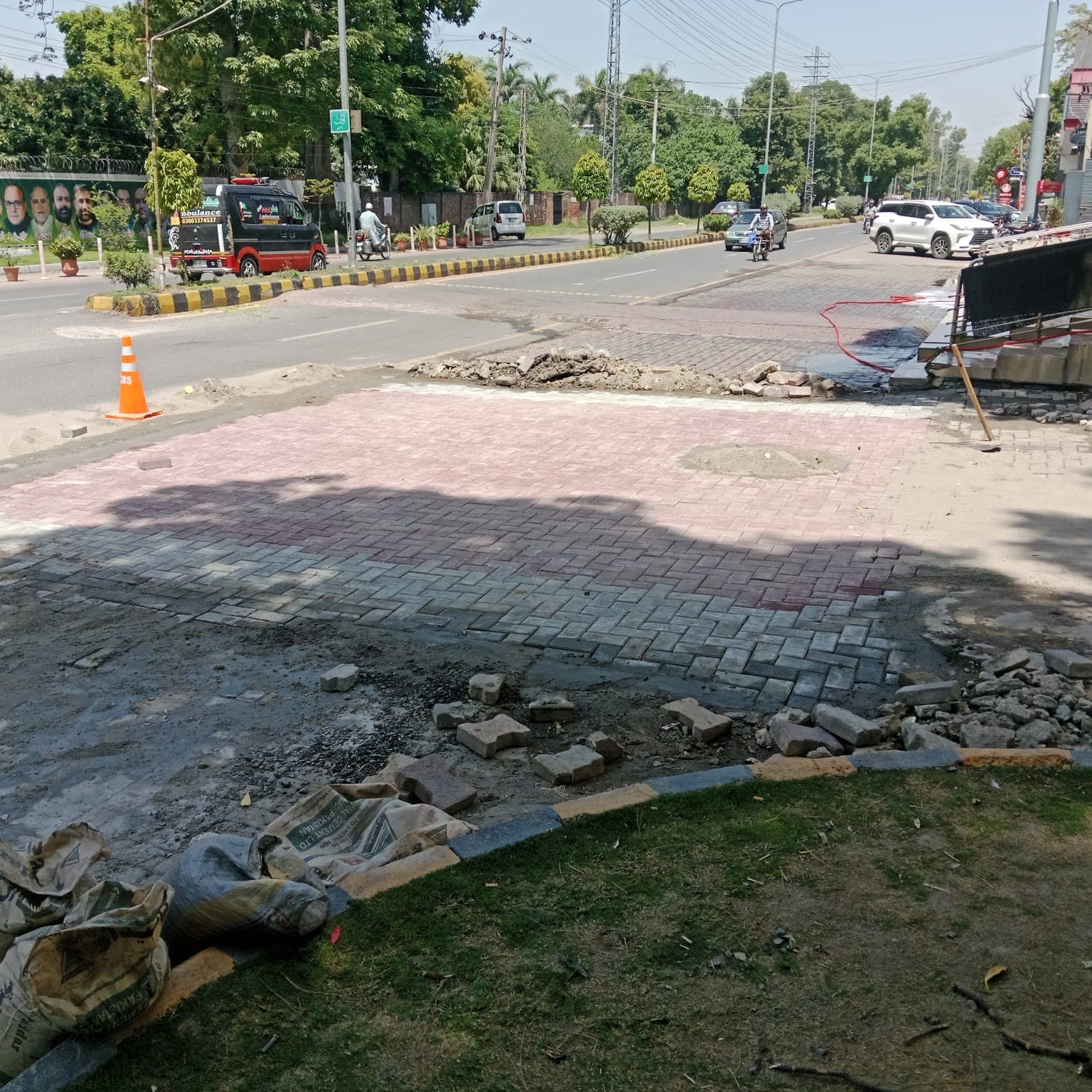 Newly relaid herringbone paving beside the road, with old tiles and cement bags still to clear