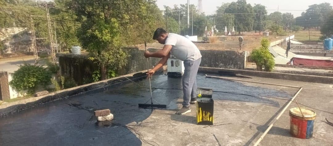 A worker spreading bitumen across a flat roof with a squeegee