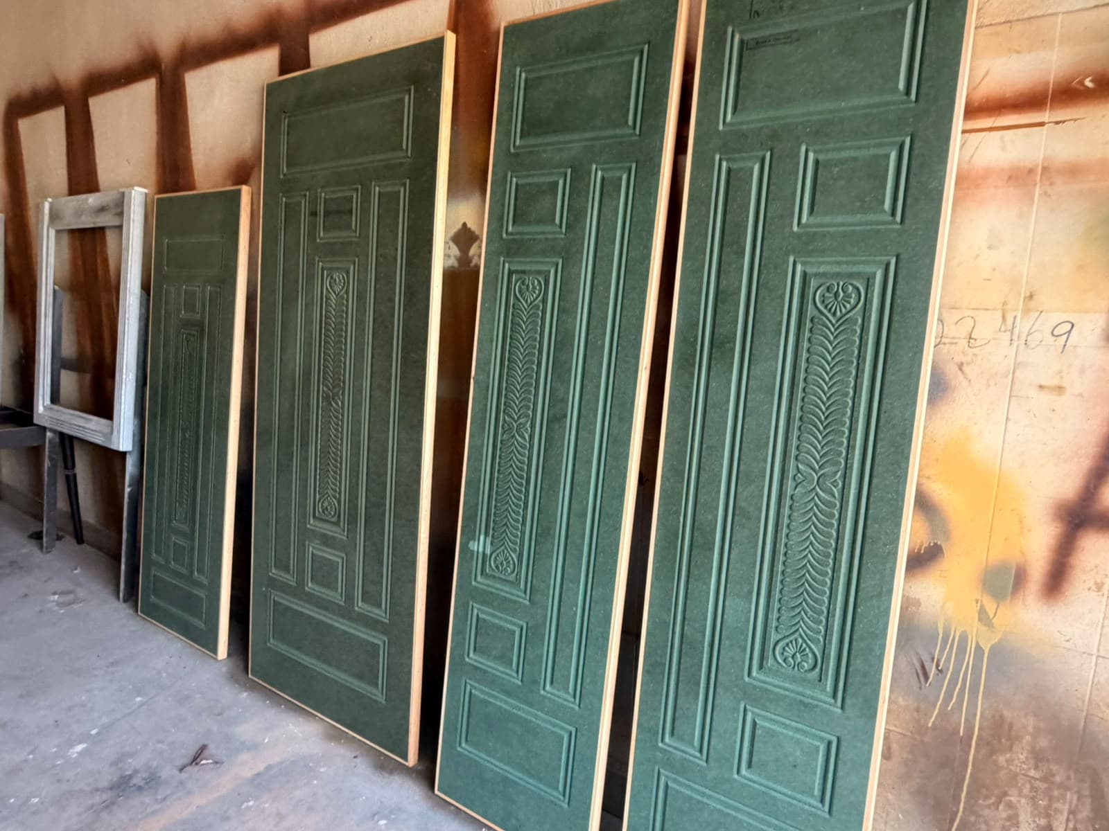 A row of carved green panel doors lined up in the workshop