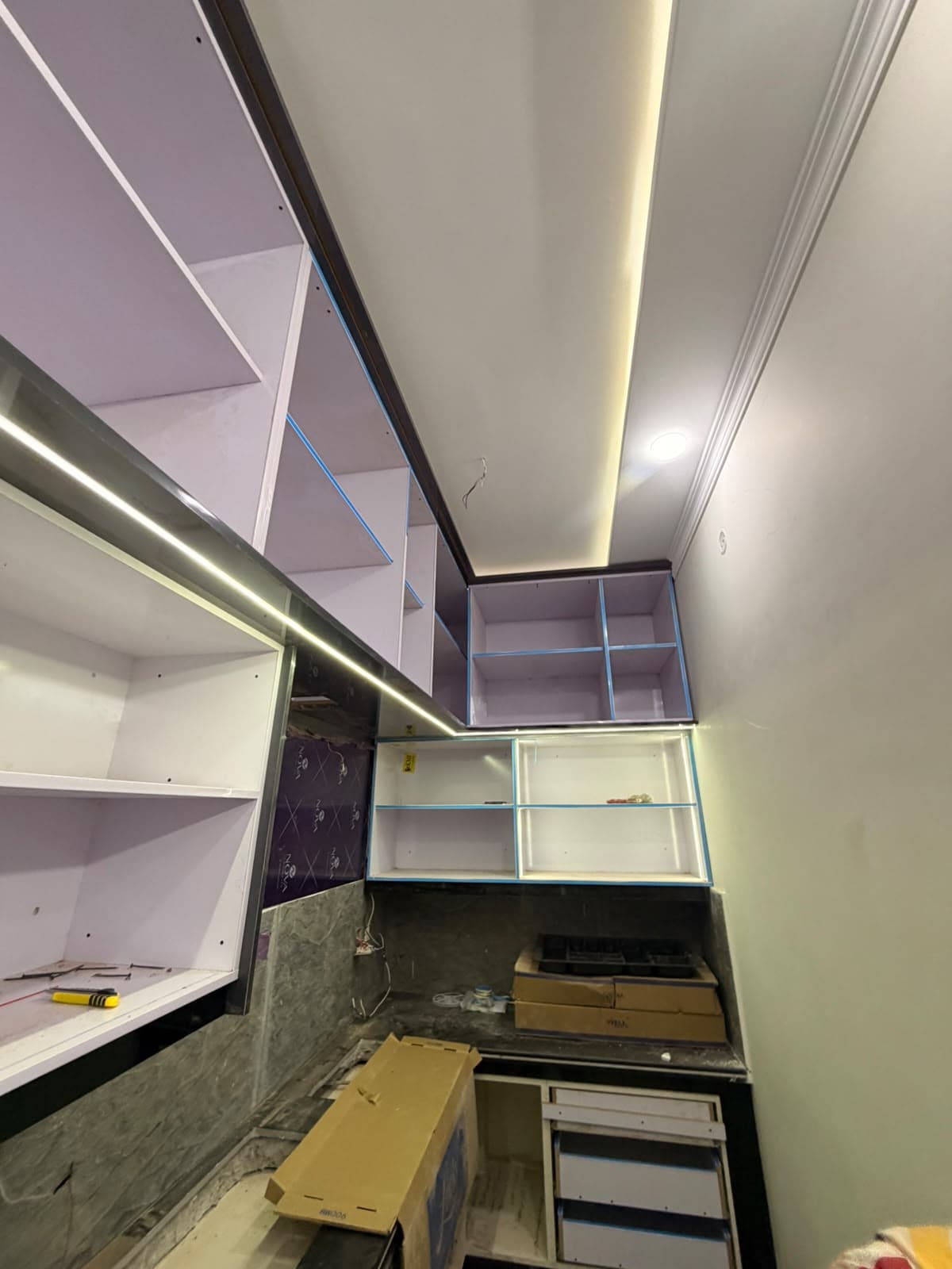 A narrow kitchen with new wall and base cabinets fitted, LED strips glowing under the wall units