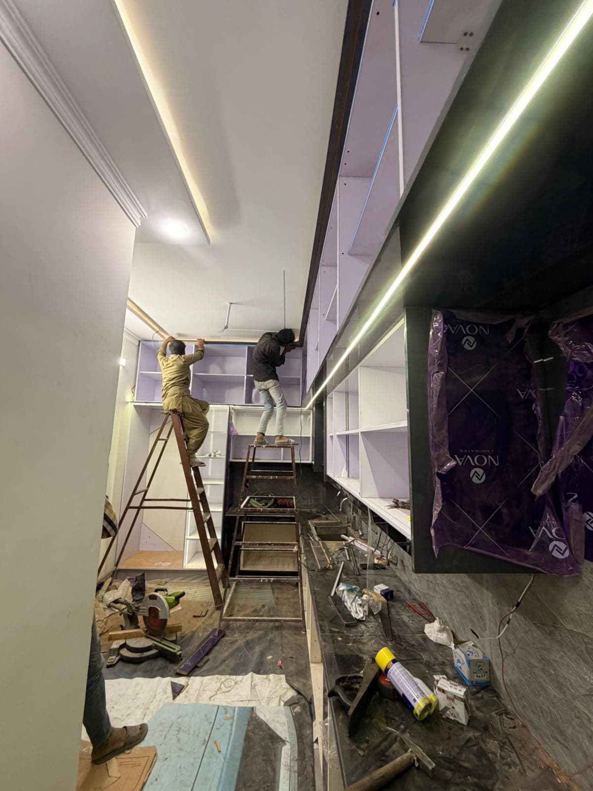 Two carpenters on ladders fitting the top row of kitchen cabinets