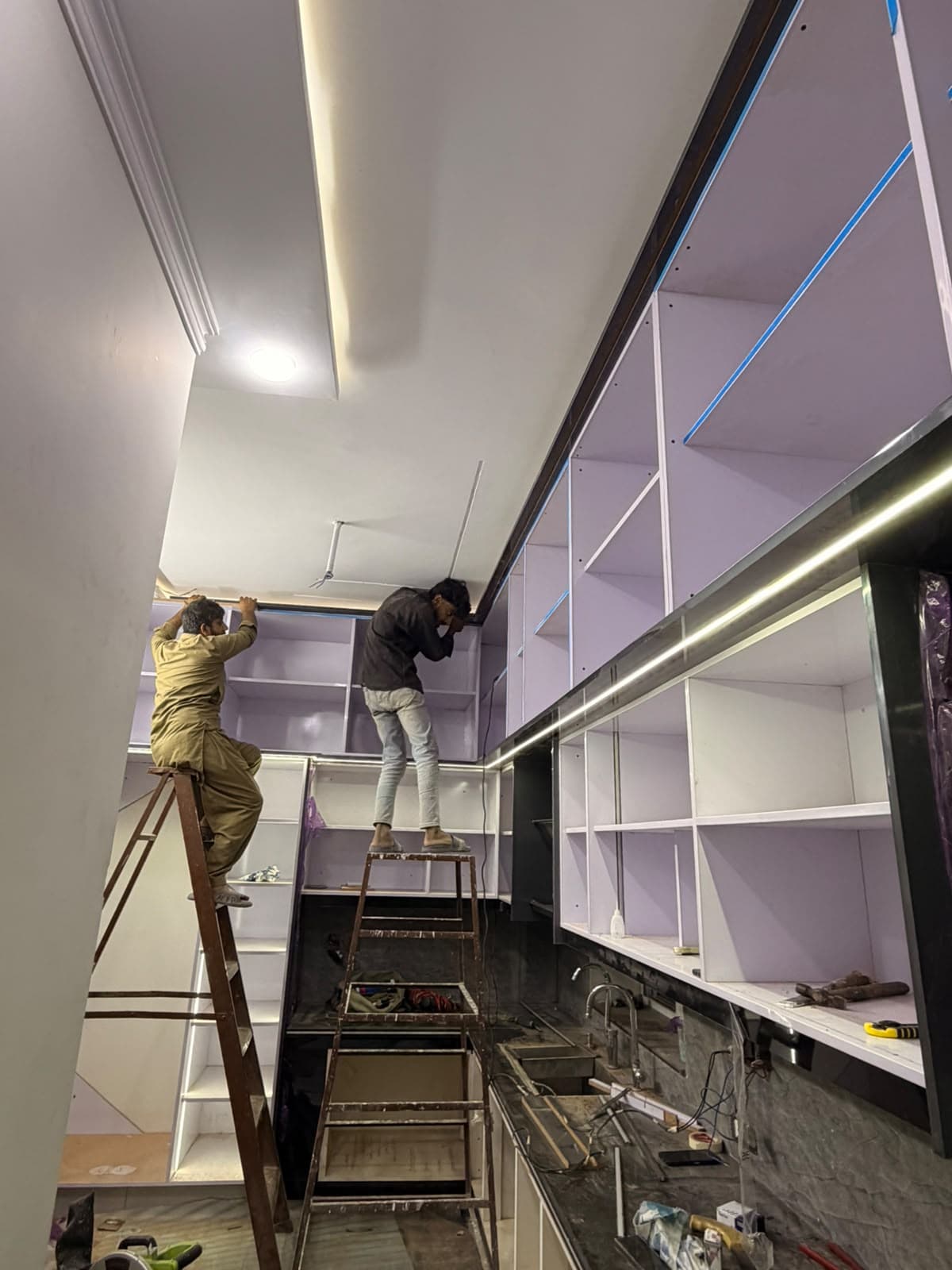 The carpenters fixing the upper cabinets along the length of the kitchen